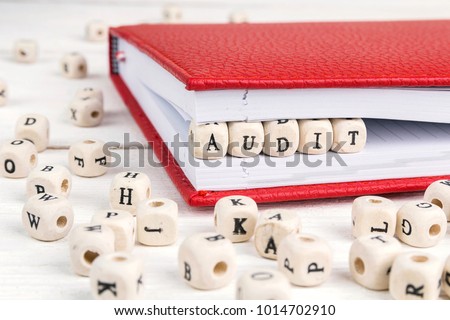 Word Audit written in wooden blocks in red notebook on white wooden table. 