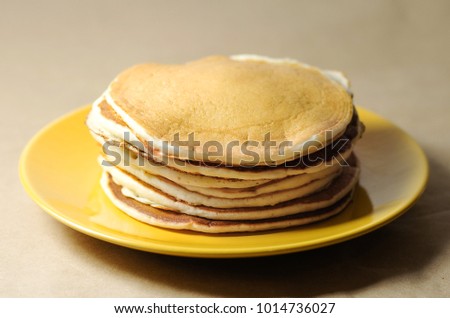 A pile of pancakes on a yellow plate on a beige background