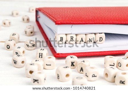 Word Brand written in wooden blocks in red notebook on white wooden table. 