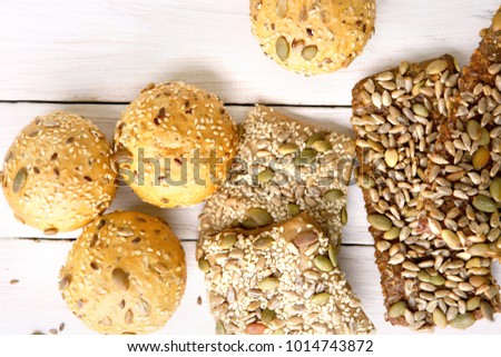 Bread buns with various seeds on white wooden table. Bread roll and breadsticks with sesame, pumpkin, sunflower, flax seeds, top view.