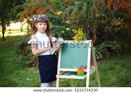 Cute schoolgirl in school uniform with a chalkboard in the park. Child painting on the easel blackboard.