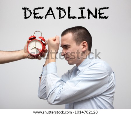 Young stressed businessman fighting against red alarm clock. Resolve problems concept. Deadline is coming. Overcome difficulties. Selective focus and shallow DOF