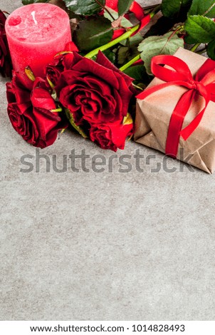 Holiday  background, Valentine's day. Bouquet of red roses, tie with a red ribbon, with wrapped gift box and red candle. On a gray stone table, copy space