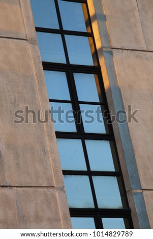 Close up view from above of a high narrow window of a modern facade building. Rectangle and square reflective elements. Pink color of the stone wall, lighted by the sunset. Abstract architectural view