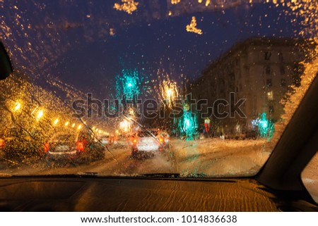 driving in night snowfall in Moscow - defocused background with view from melting snow on car windshield in evening