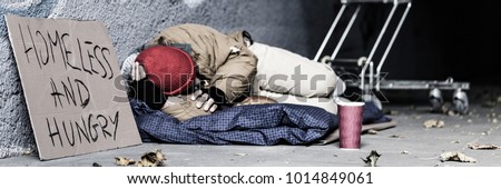 Panorama of dirty vagrant with sign "Homeless and hungry" begging in the underpass Royalty-Free Stock Photo #1014849061