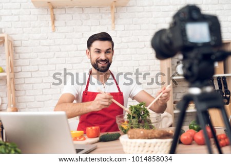 Chef in red apron presenting food ingredients for culinary podcst viewers. Vegetables and kitchen utensils.