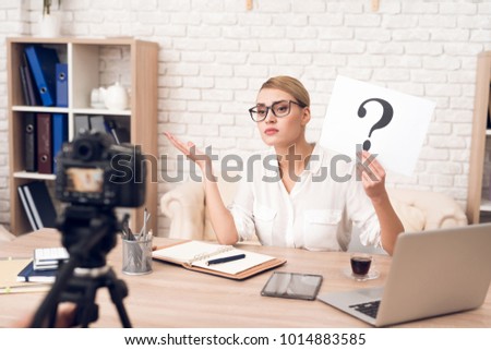 Businesswoman in blouse shows question mark at camera for business podcast.