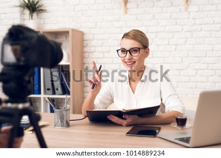 Businesswoman in blouse reads notes from notebook for business podcast.