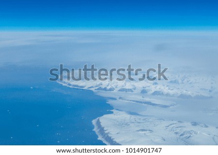 A view of a snowy landscape of Greenland, taken from the flight deck of an airplane