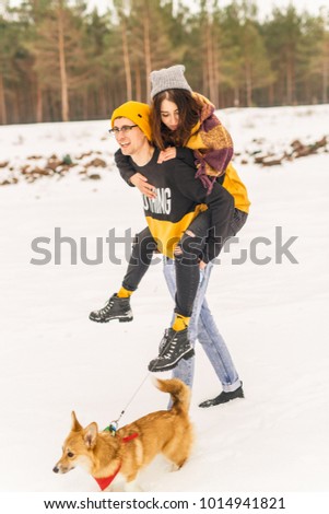 young beautiful couple in winter clothes running around with orange dog in red bandana on snow in winter