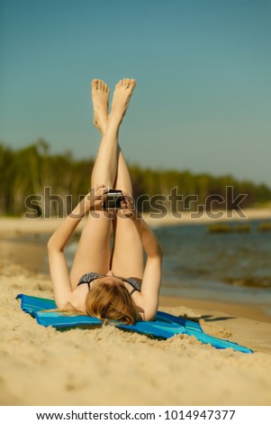 Summertime pleasures, enjoying vacation concept. Woman in bikini sunbathing and relaxing on beach, using smartphone checking social media and writing sms