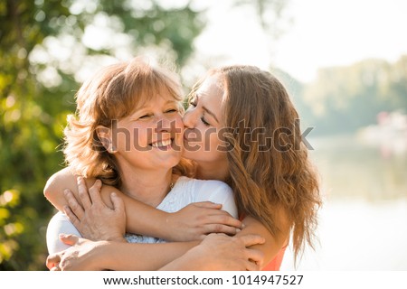 Teenage girl hugging and kissing her mother h outdoor in nature on sunny day
