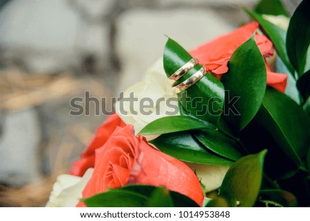 Golden wedding rings on Bridal bouquet with red and white roses