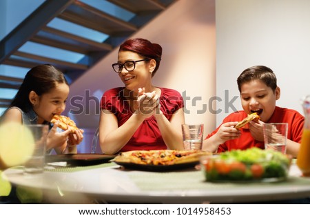 Hispanic family with mom, son and daughter having dinner at home and eating homemade pizza. Latino people with mother, boy and girl during meal. Nutrition, food and lifestyle Royalty-Free Stock Photo #1014958453