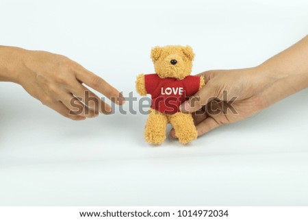 Hand giving a little teddy bear to another hand on white background.