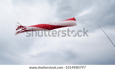 Striped Windsock Against Blue Sky With Clouds. Red White Cone Airsock In Moderate Wind. Windsock For Check Wind Way. Wind Direction Indicator At Airport Royalty-Free Stock Photo #1014980797