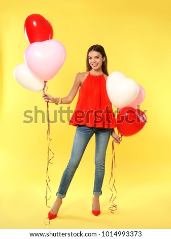Romantic young woman with heart-shaped balloons for Valentine's Day on color background
