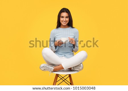 Beautiful content woman sitting on chair in studio holding cup of coffee and smiling at camera. 