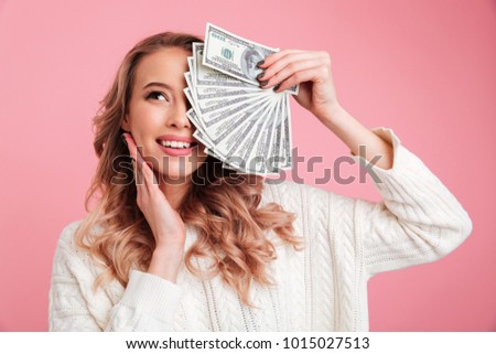 Photo of happy young woman standing isolated over pink background. Looking aside holding money.