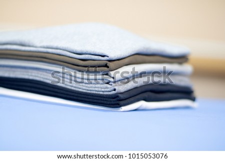 stack or pile of folded clothes, t-shirt of multiple colors perfectly ironed and folded on top of professional iron board with cream background, selective focus, laundry, retail or textile business