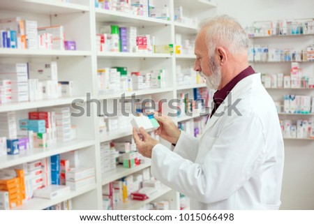 Senior male pharmacist holding a box of medications and reading labels. Side view