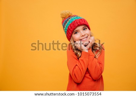 Pleased Young girl in sweater and hat reclines on her arms and looking at the camera over orange background