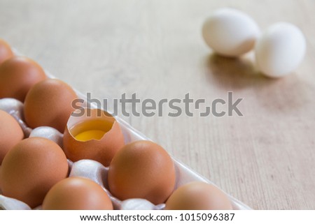 Top view of raw chicken eggs and egg yolk on a cartoon box on wooden background
