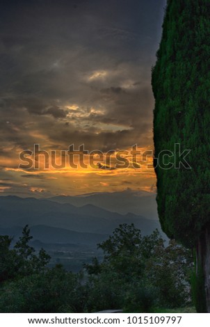 Sunset at mountain, hills in background, cloudy sky, woods in front.