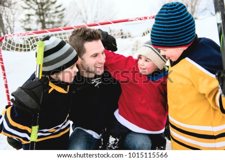 Happy funny kids playing hockey with father on street in the winter season