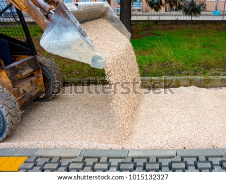 skid loader distributes grit and sand for the background of the pavement paving