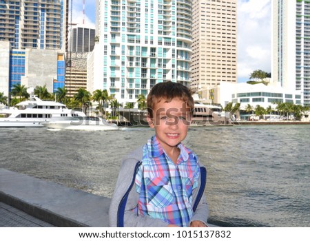 Cute smiling young boy standing near gulf,  with yachts and new buildings on background, modern lifestyle people concept