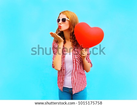 Woman sends an air kiss with a red balloon in the shape of a heart on blue background