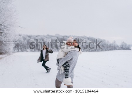 Mother and her daughters have fun near the snow-covered forest on a winter day. They ride a sled and play with snow. Winter fun mood