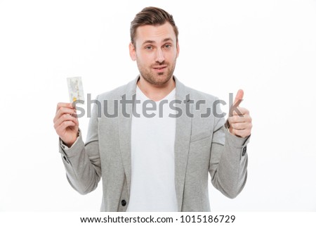 Picture of handsome young businessman standing isolated over white background. Looking camera showing thumbs up holding credit card.