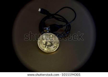 Digital kriptonite bitcoin with a USB cable on a bronze background. Abstraction review element vignetting to give emphasis to the object.