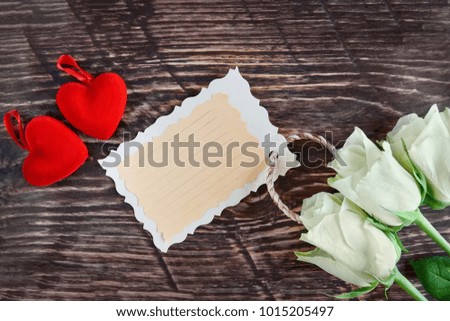 Couple red hearts, white roses and message card on wooden rustic background with copy space. Bright Valentine's day concept  with greeting card. Top view horizontal template with place for text