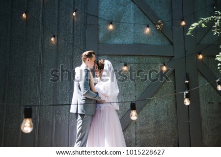 The bride and groom walk in the garden against the backdrop of a garland of light bulbs and metal doors. Wedding. The bride and groom dance