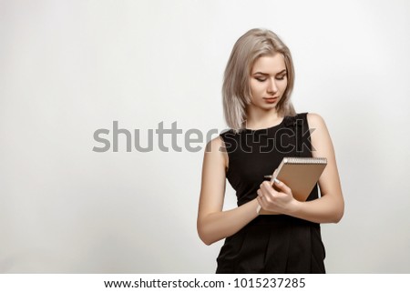 Young attractive blonde businesswoman holds black leather diary, isolated on white. Portrait of a beautiful blonde with a note and a pen in his hands