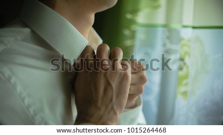 Man buttons up his white shirt standing in the front of a bright window. Clip. People, business, fashion and clothing concept - close up of man dressing up and fastening buttons on shirt at home