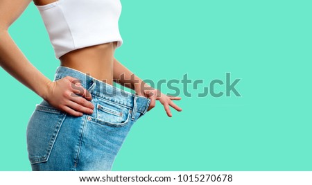 Diet concept and weight loss. Woman in oversize jeans on pastel green background Royalty-Free Stock Photo #1015270678