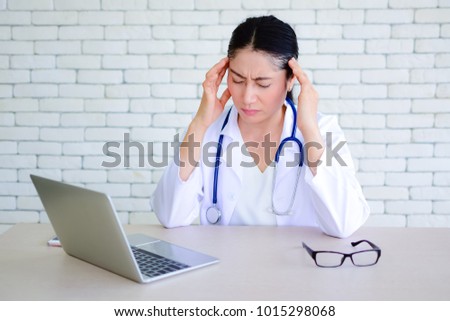 Doctor has a headache sitting at the desk. Strong headache is very problematic. Strong headache during work at the desk in the hospital. Feeling stressed. Doctor touching her head.