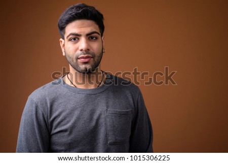Studio shot of young handsome Indian man against brown background
