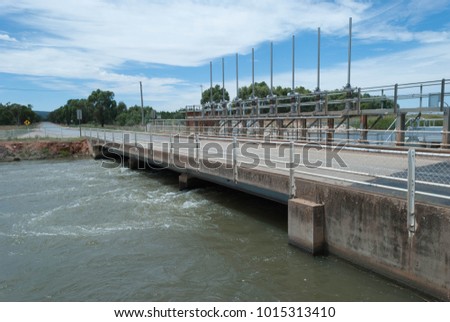 small bridge spaniing an irrigation channel with flowing water beneath and clouds in the sky on a sunny day