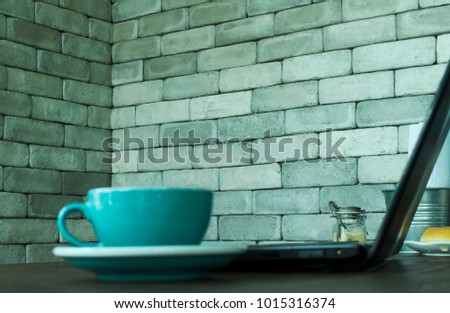 Defocus of Blurry blue coffee cup and Laptop computer with gray brick wallpaper backgrounds