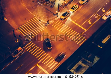 Cars and people on road intersection with signal lights and crosswalks at night time in the city street