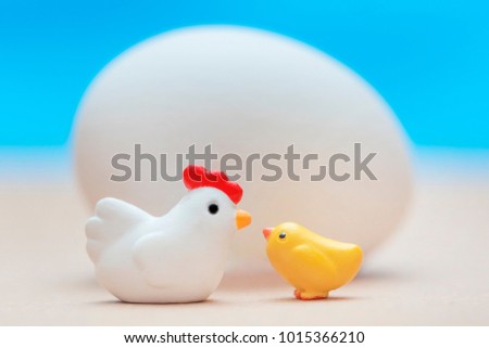 White little toy chicken with a yellow chick near a big white egg