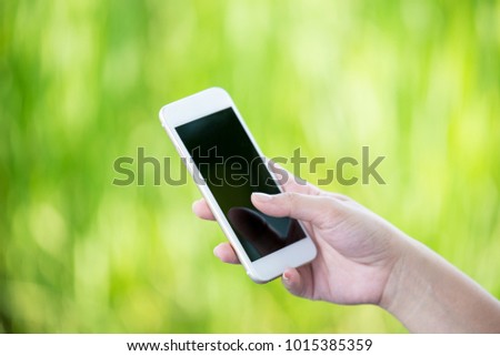 Woman hand holding a smart phone outdoor with a green background