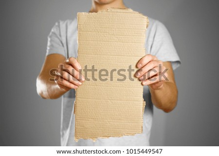 A young guy in a white t-shirt holding a piece of cardboard. Prepared for your text.