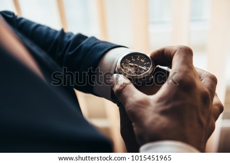 a stylish mechanical watch on the arm of a man dressed in a blue jacket with a white shirt that watches the time on the clock holding the clock by hand Royalty-Free Stock Photo #1015451965